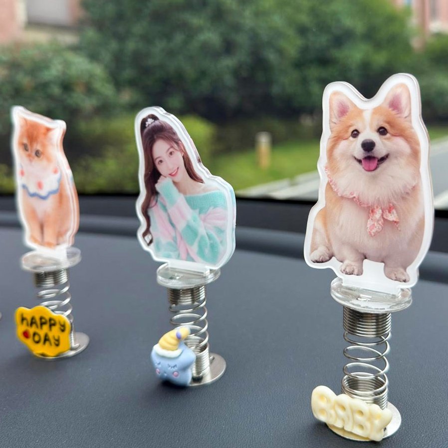 Three custom photo spring bobbleheads displayed on a car dashboard - a cute kitten, a young woman, and a smiling corgi dog