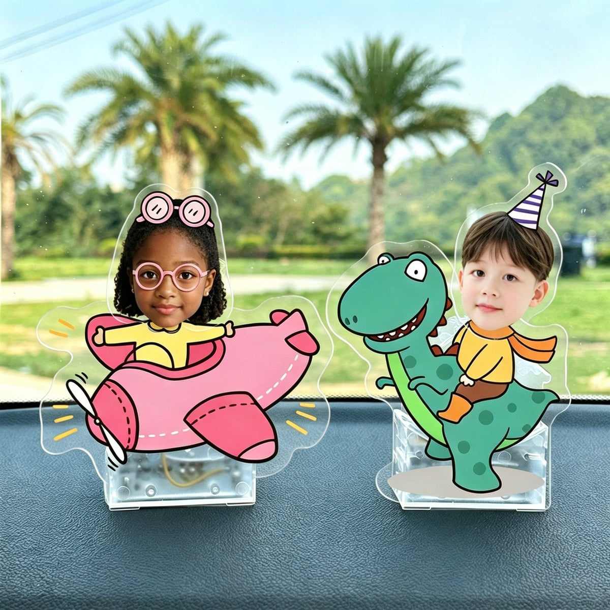 Custom photo wobble figures on a car dashboard - a kid riding a pink airplane and a kid riding a green dinosaur, each
